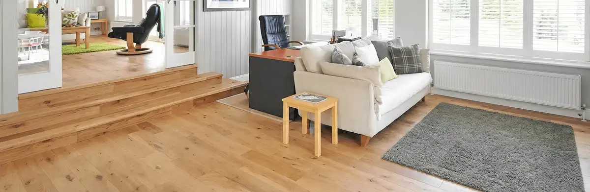 A modern living room with professionally installed laminate flooring, a beige sofa, a small side table, a gray rug, and large windows with white shutters in Fargo, ND